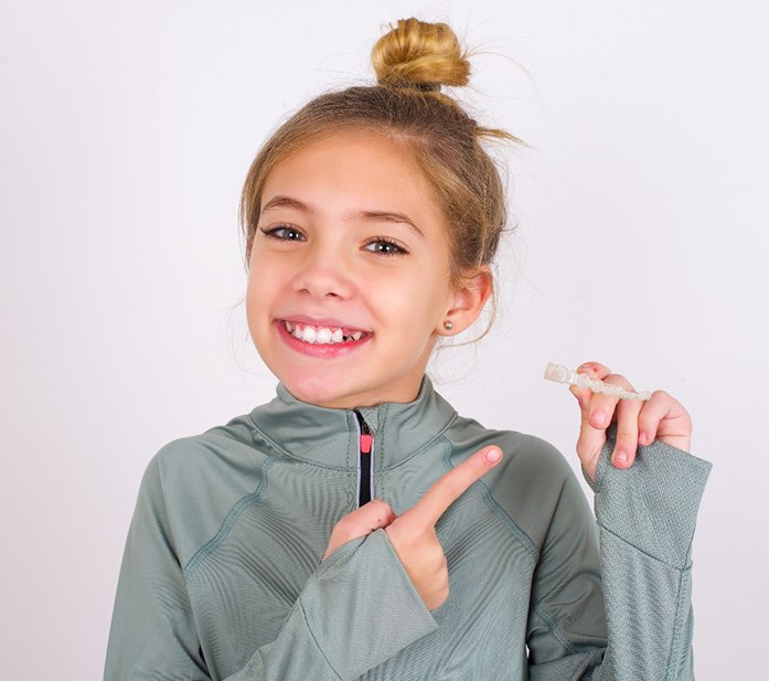 Teen girl smiling and pointing to clear aligner