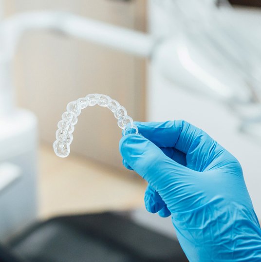 Dentist with blue glove holding clear aligner