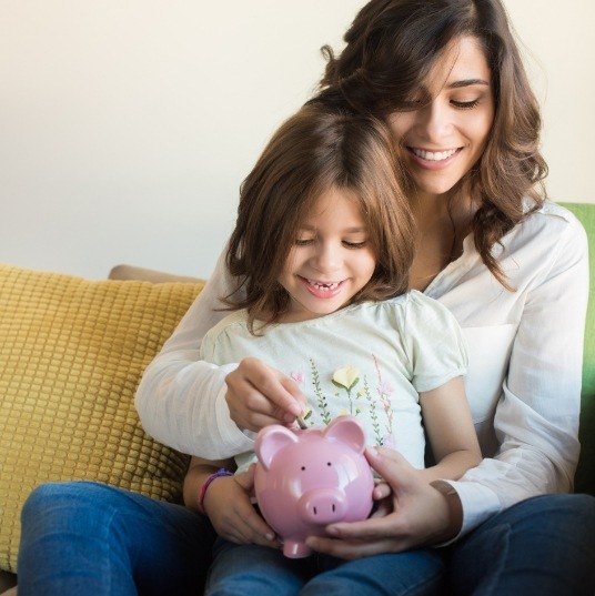 Mother and daughter placing coins in a piggy bank
