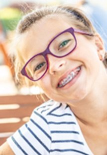 Child with braces and glasses smiling outside