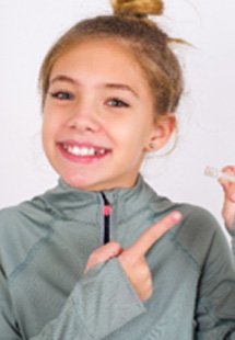Young girl smiling while holding clear aligners