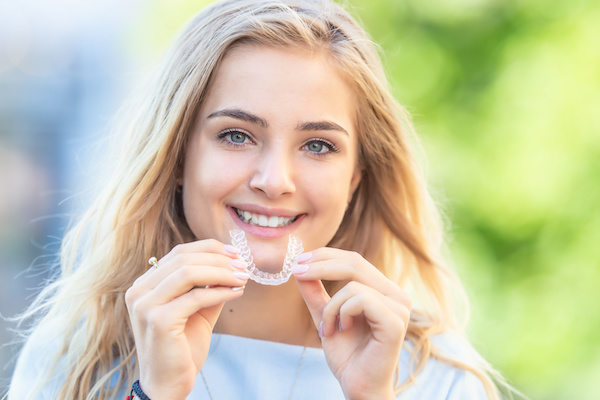 young woman smiling holding Invisalign aligner